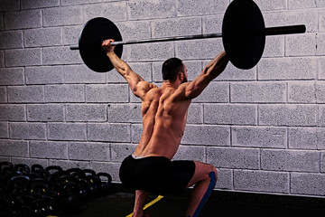 Athletic shirtless male doing squats with a barbell under his head.