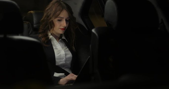 Attractive Business woman works at a laptop in the backseat of car