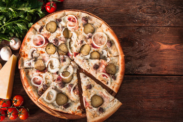 Fresh homemade pizza with cut slice served on wooden table with ingredients top view, with copy space for text. Italian cuisine.