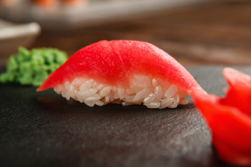 Close up view of delicious and tasty one sushi nigiri with fresh tuna fillet, served on black slate with ginger and wasabi. Japanese cuisine, healthy seafood.