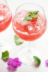 Strawberry cocktail with ice in a wine glass on a white background with mint leaves and flowers.