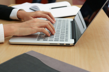 working woman who wear black suit and white shirt is typing something on keyboard of laptop