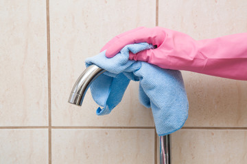 In the kitchen, hand in protective glove with rag washing and polishing dirty water tap and sink. Maid or housewife cleans house. General cleaning or regular wash up.
