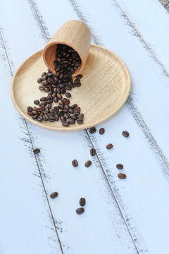 coffee beans were piil out of wooden cup on wood plate on white table background