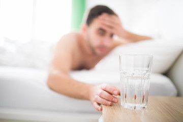 Handsome Man wake up with head pain suffers from headache and extend to get a glass of water in his...