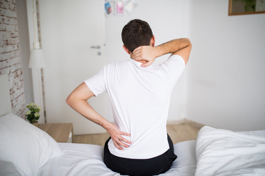 Man suffering from back pain at home in the bedroom. Uncomfortable mattress and pillow causes back pain.