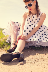 Pinup Girl mit Petticoat und Sonnenbrille sitzt am Wegrand