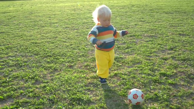 One and a half year old boy joyfully chases the ball on the field