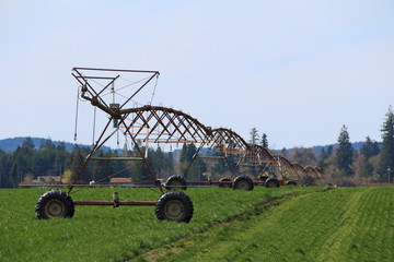 Full Three-Quarter Left Side of Frame Viewpoint, Overhead Commercial Agricultural Irrigation System on Green Farm Field, Blue Sky with Wisp of White Clouds, Daytime - Oregon, USA (HDR Image)
