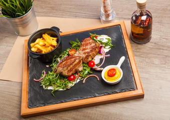 Roasted pork knuckle served on a black board with French fries and salad