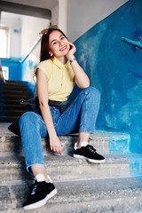 Obraz na płótnie Canvas Young teenage girl sitting on stairs of house entrance, wear on yellow t-shirt, jeans and sunglasses.