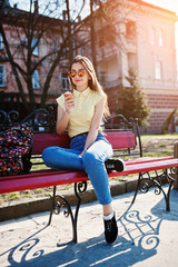 Young teenage girl sitting on bench with ice cream at hands, wear on yellow t-shirt, jeans and sunglasses.