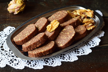 Homemade sweet chocolate sausage cut in pieces on a metal tray and on a wooden background