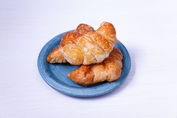 Fresh croissants. Delicious buttered roll in blue plate. French cuisine. On white wooden rustic background.