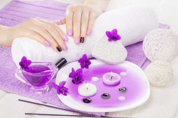 Obraz na płótnie Canvas beautiful purple manicure with violet, candle and towel on the white wooden table.