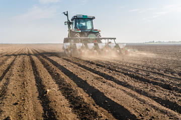 Fototapeta premium Farmer with tractor seeding - sowing soy crops at agricultural field in spring