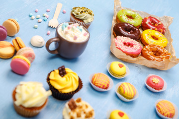 Cupcakes, macaroons and donuts. Mug with whipped cream and marshmallows. Almond macaron cookies. Sweet dessert.