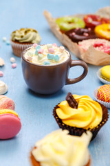 Cupcakes, macaroons and donuts. Mug with whipped cream and marshmallows. Almond macaron cookies. Sweet dessert.