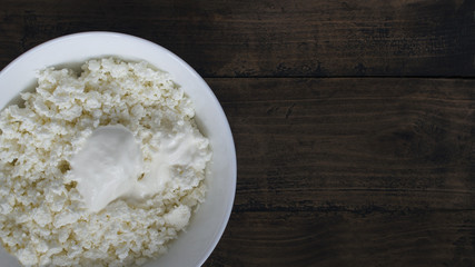 White plate with rustic grainy cottage cheese and sour cream on a wooden table