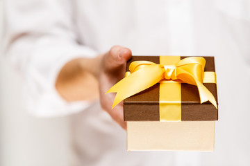 Male hand holding a gift box. Present wrapped with ribbon and bow. Christmas or birthday package. Man in white shirt.