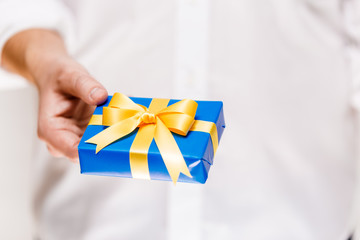 Male hand holding a gift box. Present wrapped with ribbon and bow. Christmas or birthday blue package. Man in white shirt.