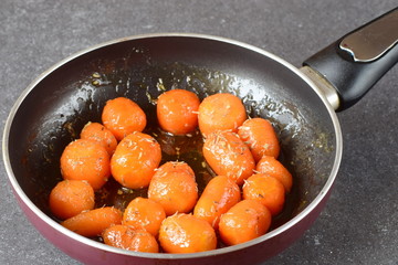 Honey glazed baby carrots with sea salt and thyme in a frying pan on a grey abstract background. Healthy eating concept. Fastening food. Healthy meal