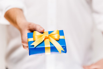 Male hand holding a gift box. Present wrapped with ribbon and bow. Christmas or birthday blue package. Man in white shirt.