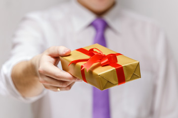 Male hand holding a gift box. Present wrapped with ribbon and bow. Christmas or birthday package. Man in white shirt and necktie.