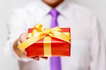 Male hand holding a gift box. Present wrapped with ribbon and bow. Christmas or birthday red package. Man in white shirt and necktie.