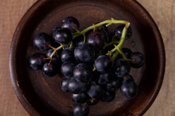 Dark grapes bunch. Ripe grape fruit on rustic plate. On wooden background.