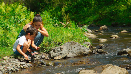 Mother with her son are sitting near a stream