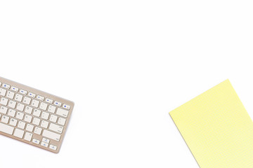 Desk in the office with a keyboard and a yellow Notepad on a white background. Top view with copy space.