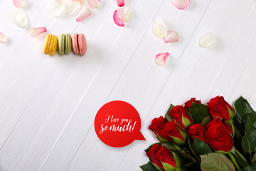 Macaroon cakes with bouquet of red roses. Different types of macaron. I love you speech bubble. White wooden rustic background.