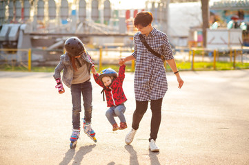 Active young mother walks in the park with the kids, laugh, ride on rollers