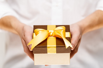 Male hands holding a gift box. Present wrapped with ribbon and bow. Christmas or birthday package. Man in white shirt.