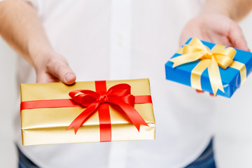 Male hands holding a gift boxes. Presents wrapped with ribbon and bow. Christmas or birthday blue, golden packages. Man in white shirt.