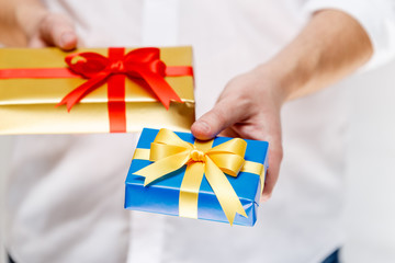 Male hands holding a gift boxes. Presents wrapped with ribbon and bow. Christmas or birthday blue, golden packages. Man in white shirt.