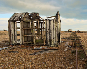 A derelict wooden shed on a beach with abandoned fishing boat in the background.
