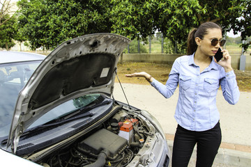 A woman with a broken car, talking on the phone, waits for assistance