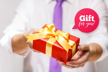 Male hands holding a gift box. Present wrapped with ribbon and bow. Gift for you speech bubble. Man in white shirt and necktie.