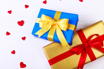 Gift boxes with red satin hearts. Presents wrapped with ribbon and bow. Christmas or birthday golden and blue paper package. On white table.