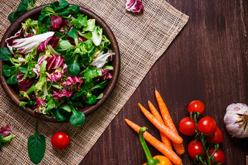 Provence salad. Leaves of endive or chicory, lamb and rose salad. Cherry tomatoes and carrot. Raw vegetables. On wooden table.