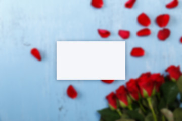 Business card mockup. Petals of red roses on blue painted rustic background. Fresh natural bouquet of flowers.