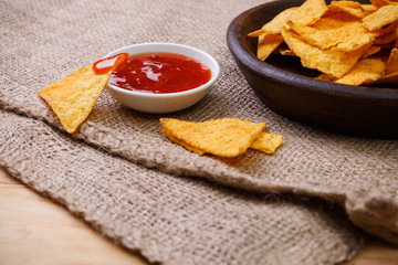 Nachos chips. Delicious salty tortilla with sweet salsa or chilli sauce on sackcloth background. Snack on rustic plate.