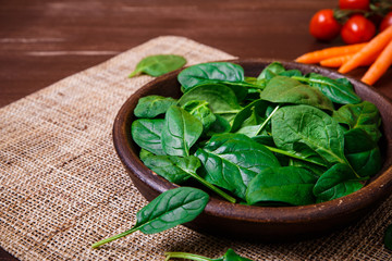 Spinach leaves in bowl. Carrot and cherry tomatoes. Raw fresh vegetable. Fresh natural plant leaf. Organic bio food on rustic wooden table.