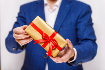 Male hands holding a gift box. Present wrapped with ribbon and bow. Christmas or birthday package. Man in suit and white shirt.