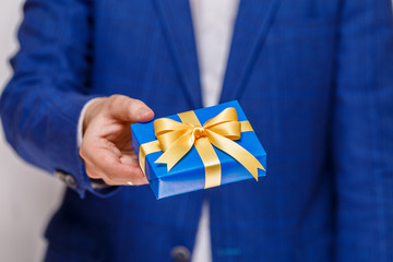 Male hand holding a gift box. Present wrapped with ribbon and bow. Christmas or birthday blue package. Man in suit and white shirt.