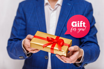 Male hands holding a gift box. Present wrapped with ribbon and bow. Gift for you speech bubble. Man in suit and white shirt.