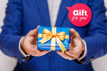 Male hands holding a gift box. Present wrapped with ribbon and bow. Gift for you speech bubble. Man in suit and white shirt.
