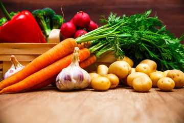 Vegetables. Potatoes, carrot and red pepper. Garlic and brocoli. Onion and radish. Wooden basket on rustic table.